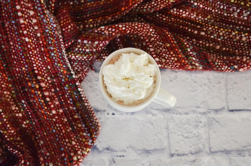 Single origin chai latte recept in een witte mok met slagroom, omringd door een kleurrijke sjaal.