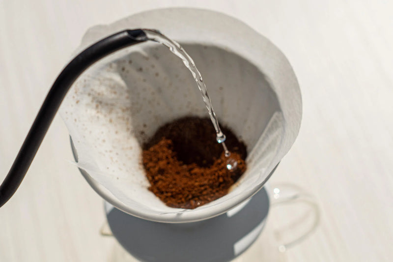 beste pour-over apparatuur thuisbarista met een straal water die op gemalen koffie valt.