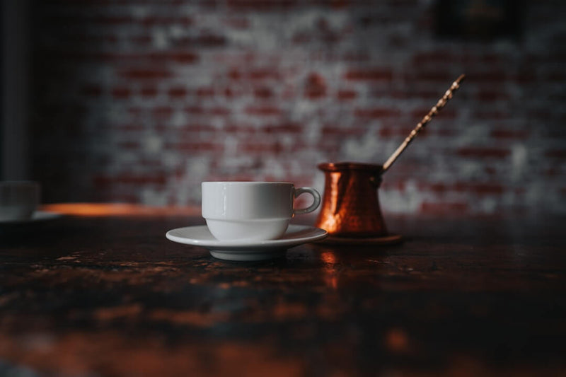 Koffie en gezondheid: een kopje koffie op een houten tafel met een bronzen pot en een lepel.
