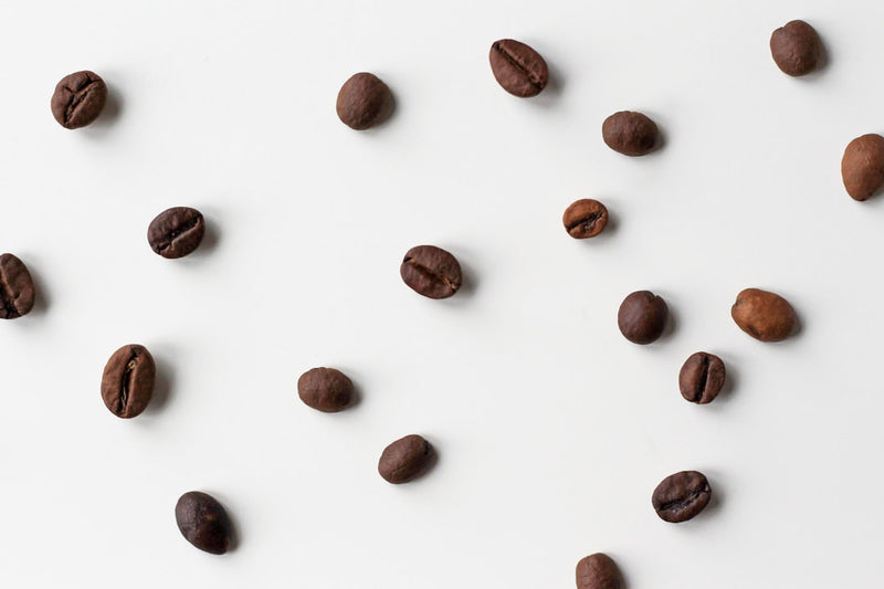Koffiebonen verspreid op een witte achtergrond, illustratief voor single origin of blend koffie branden.